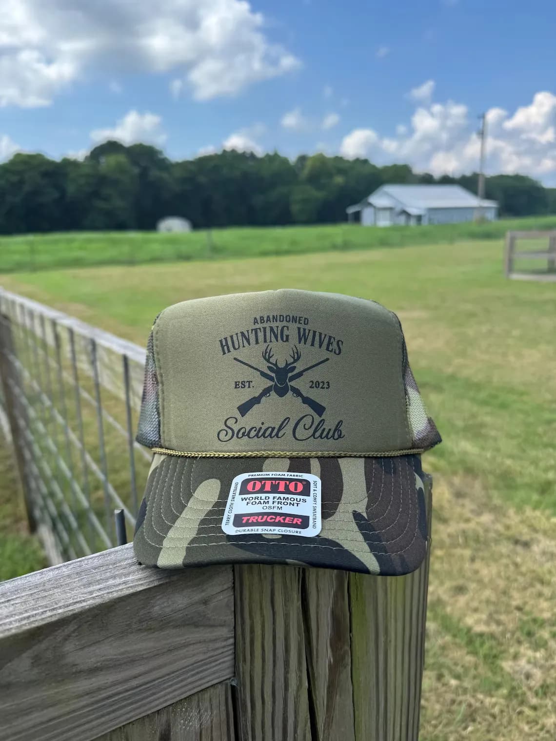 Hunting Wives Social Club logo on an olive green OTTO foam front trucker hat, featuring 100% manual digitizing for a clean, non-puckered finish.